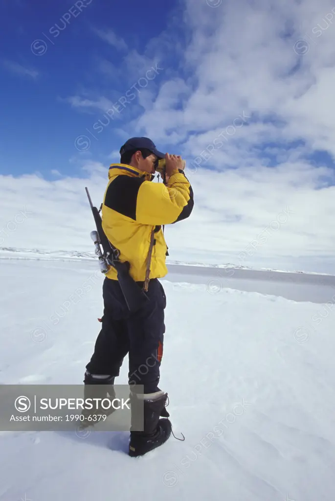 Young Inuit hunter scans horizon at ice flow edge near village of Kimmirut, Baffin Island, Nunavut, Canada