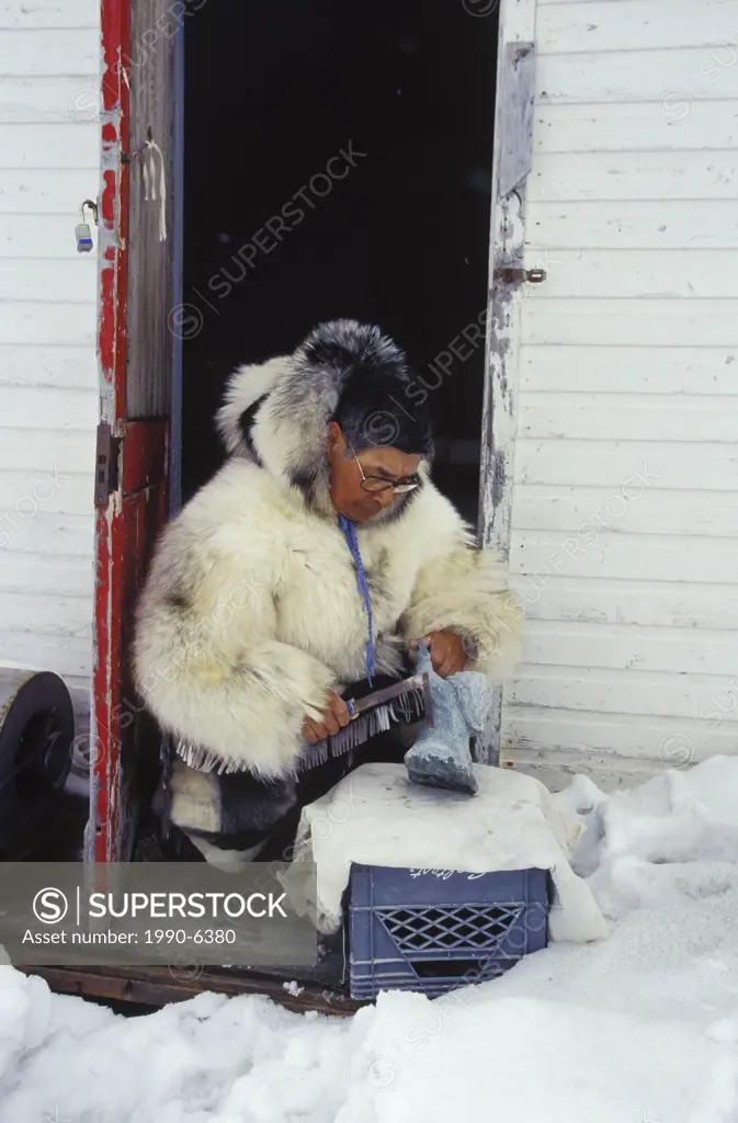 Inuit elder works on soapstone carving in traditional clothing, Kimmirut, Baffin Island, Nunavut, Canada