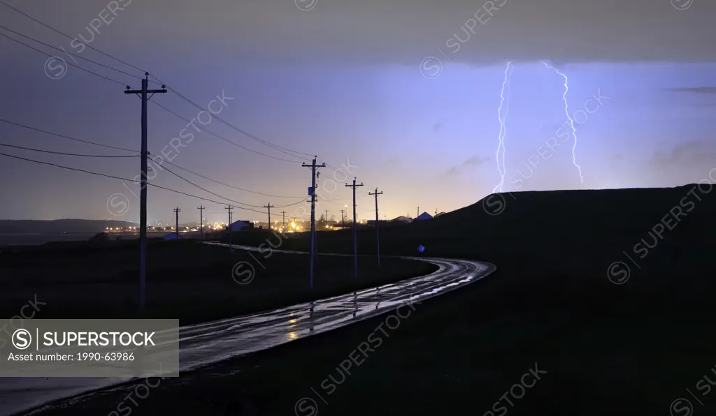 Wet road and utility poles illuminated by lightning strike in Eastern Passage, Nova Scotia, during an evening storm.