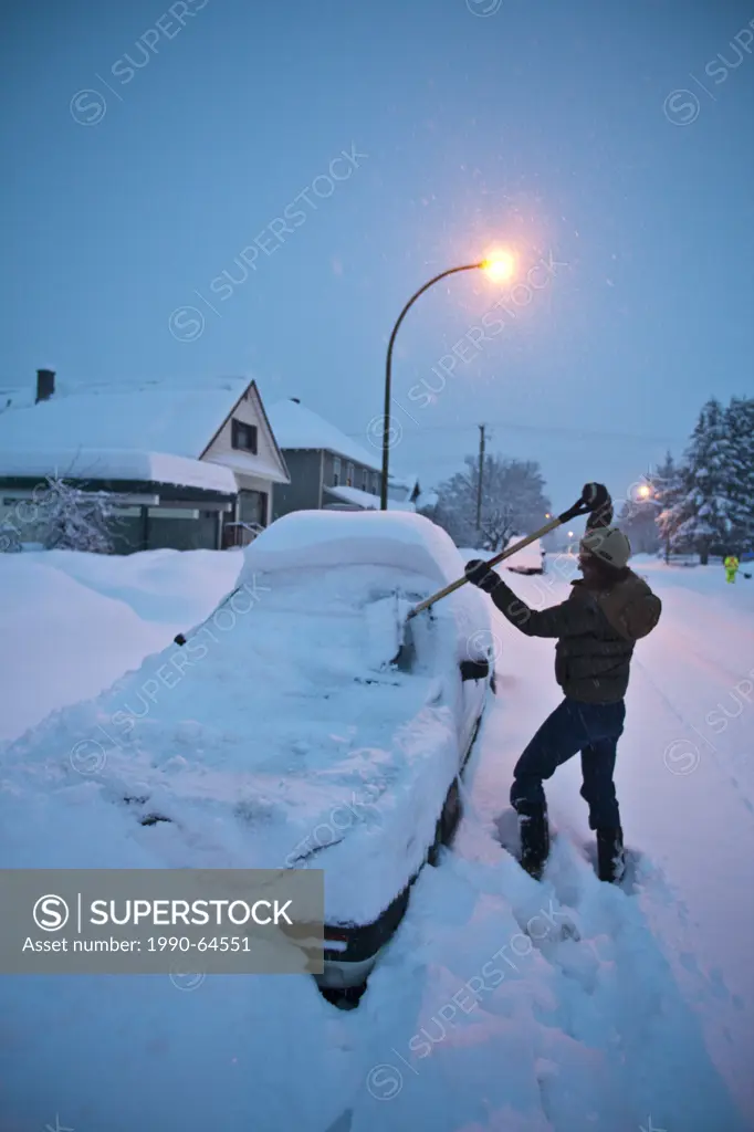 A woman shovels snow off her vehicle before work. Revelstoke, BC