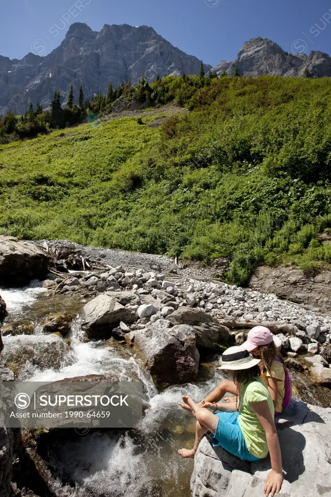 Two young girls relax by stream on Mountain Lakes Trail near Fernie, BC, Canada.