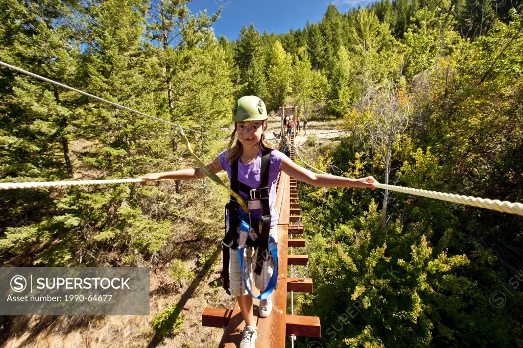 Young girl walks on suspension bridge at Oyama Zipline, Okanagan Valley, BC, Canada.