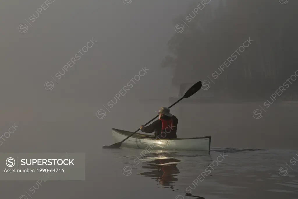 Man paddles solo canoe on Oxtongue Lake, Muskoka, Ontario.