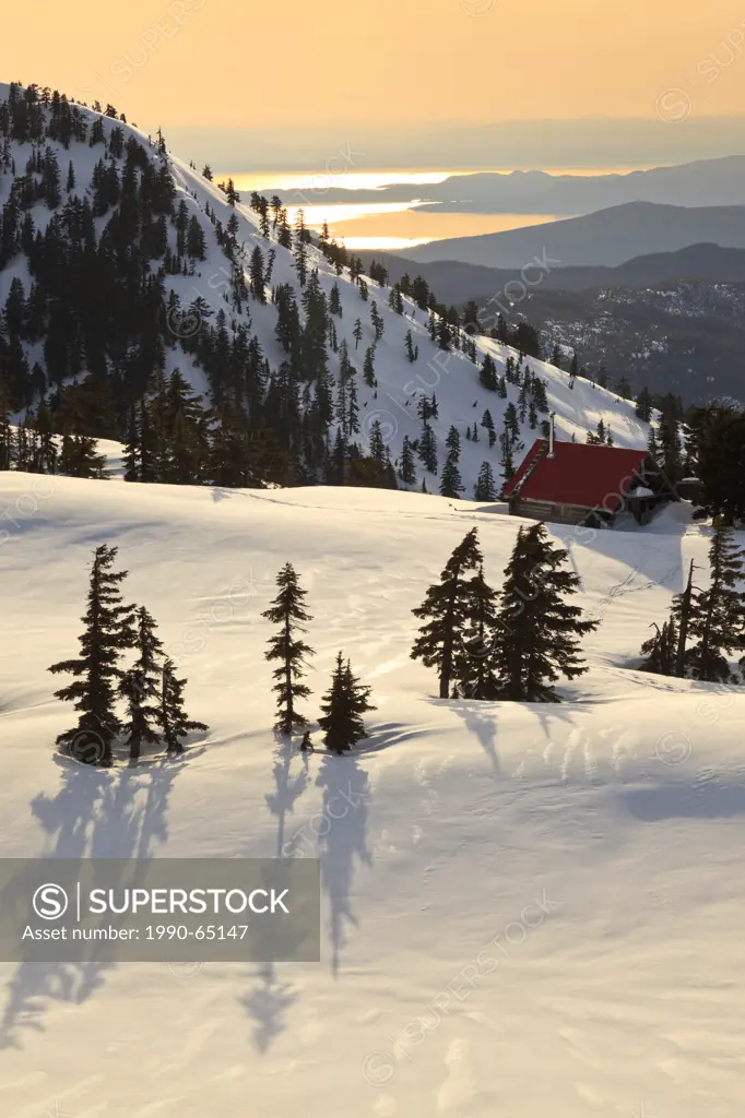 The sun sets on Mt. Steele cabin in Tetrahedron Provincial park on the Sunshine Coast with the Strait of Georgia and Vancouver Island as backdrop, Bri...