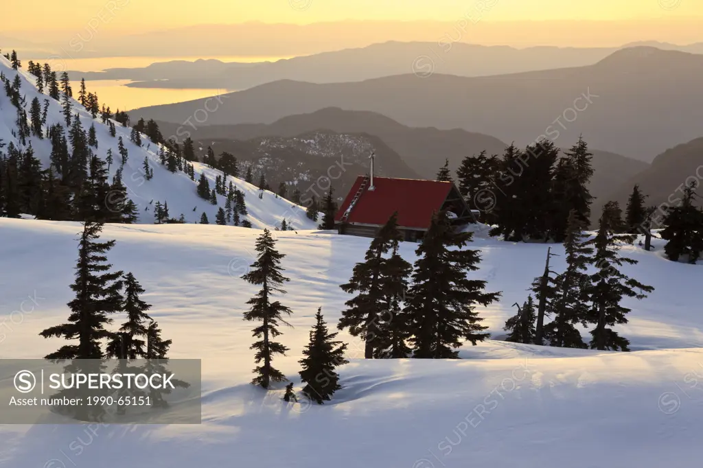 The sun sets on Mt. Steele cabin in Tetrahedron Provincial park on the Sunshine Coast with the Strait of Georgia and Vancouver Island as backdrop, Bri...
