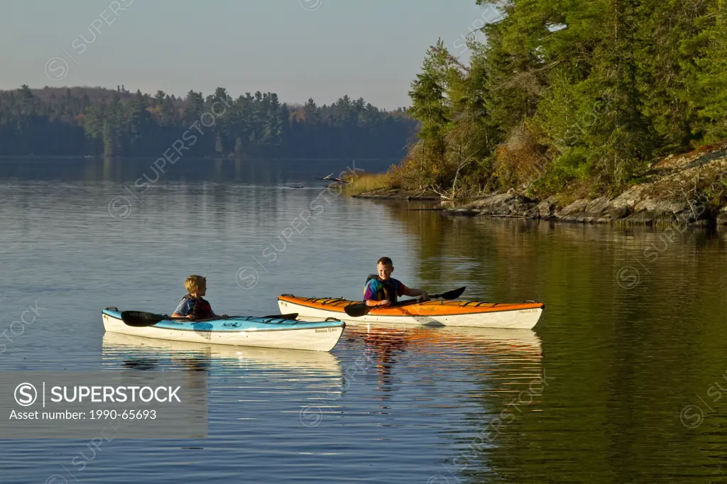 Two young boys enjoy early morning paddle in kayaks on Source Lake, Algonquin Park, Ontario, Canada.