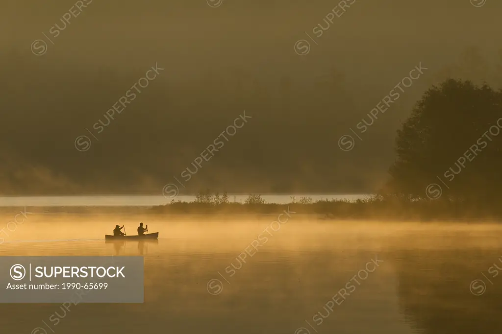 Two men paddle canoe at sunrise on Oxtongue Lake, Muskoka, Ontario, Canada.