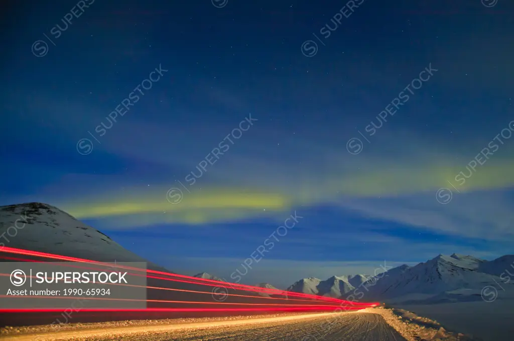 Truck passing on the James Dalton Highway Haul Road along the Alaskan Oil Pipeline under a star filled sky with dancing northern lights Aurora boreali...