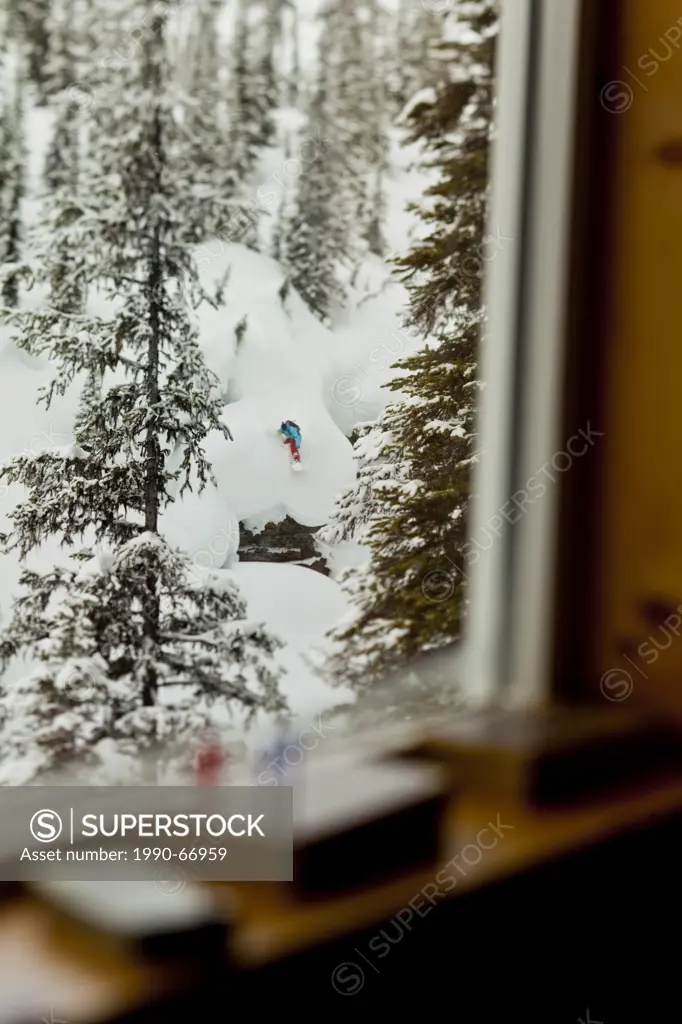 A backcountry snowboarder drops a cliff while framed through a lodge window, Icefall Lodge, Golden, BC