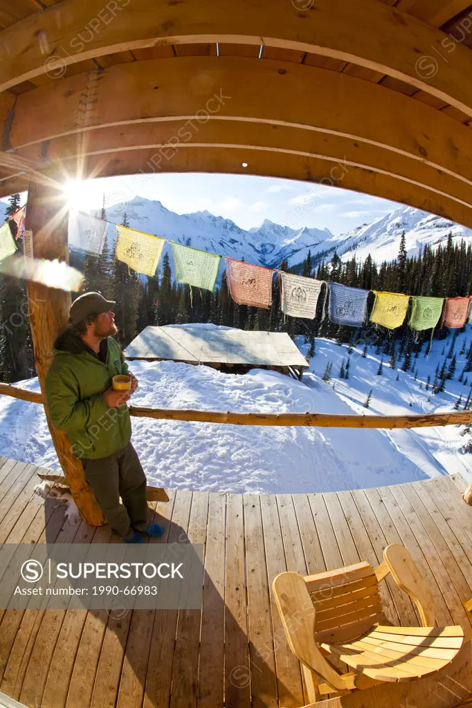 A man enjoying early morning sunrise and a coffee at a backcountry ski lodge. Icefall Lodge, Golden, BC