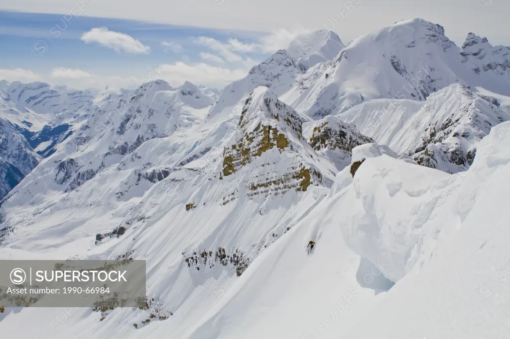 A male backcountry skiers rips a big line under a giant cornice in the Candian Rockies. Icefall Lodge, Golden, BC
