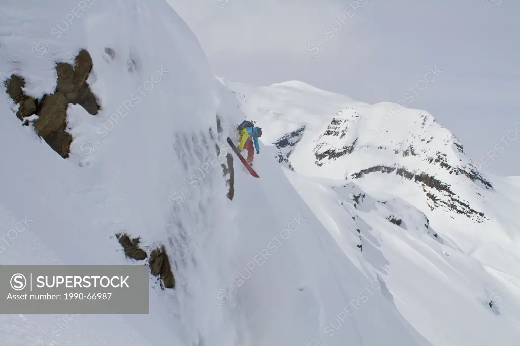 A male splitboarder drops a cliff with his sluff in canadian rockies backcountry. Icefall Lodge, Golden, BC