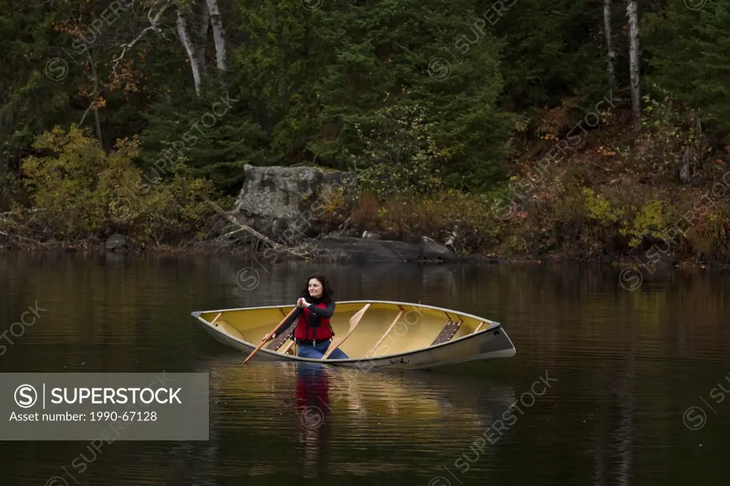 Young/middle_aged woman paddling canoe in serene setting on Oxtongue Lake, Muskoka, Ontario, Canada.