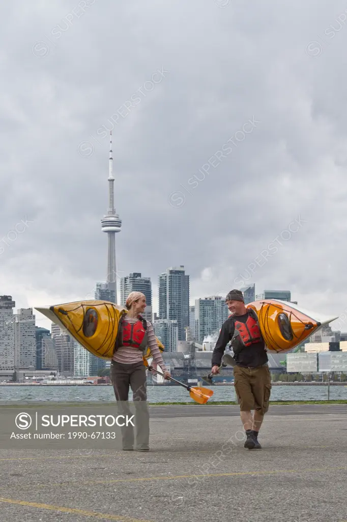 Young couple carry kayaks from Lake Ontario, Toronto waterfront, Toronto, Ontario, Canada.