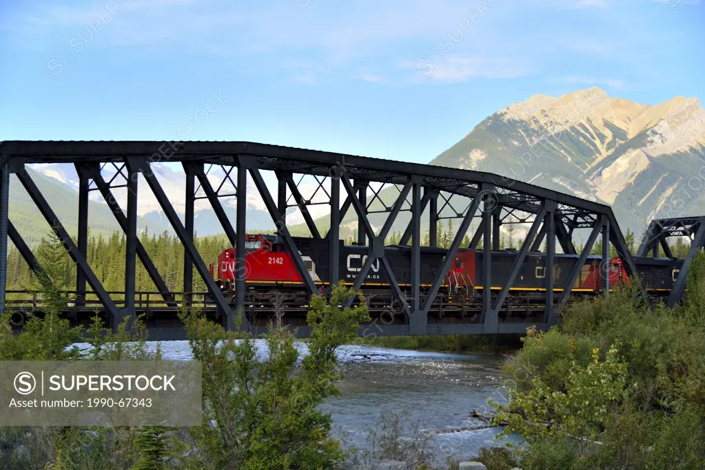 Canadian National Freight Train engines pulling a load of rail cars west on a train bridge over the Snaring river in the rocky mountains of Jasper Nat...