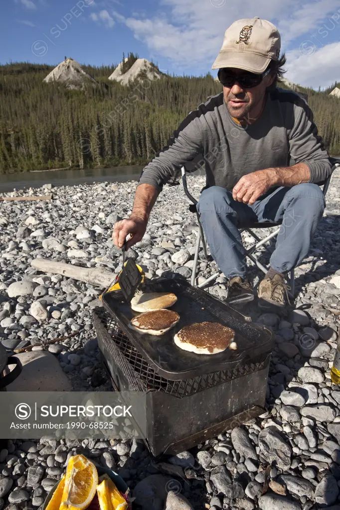 MIddle_aged man cooking pancakes over firebox while camped on Nahanni River, Nahanni National Park Preserve, NWT, Canada.