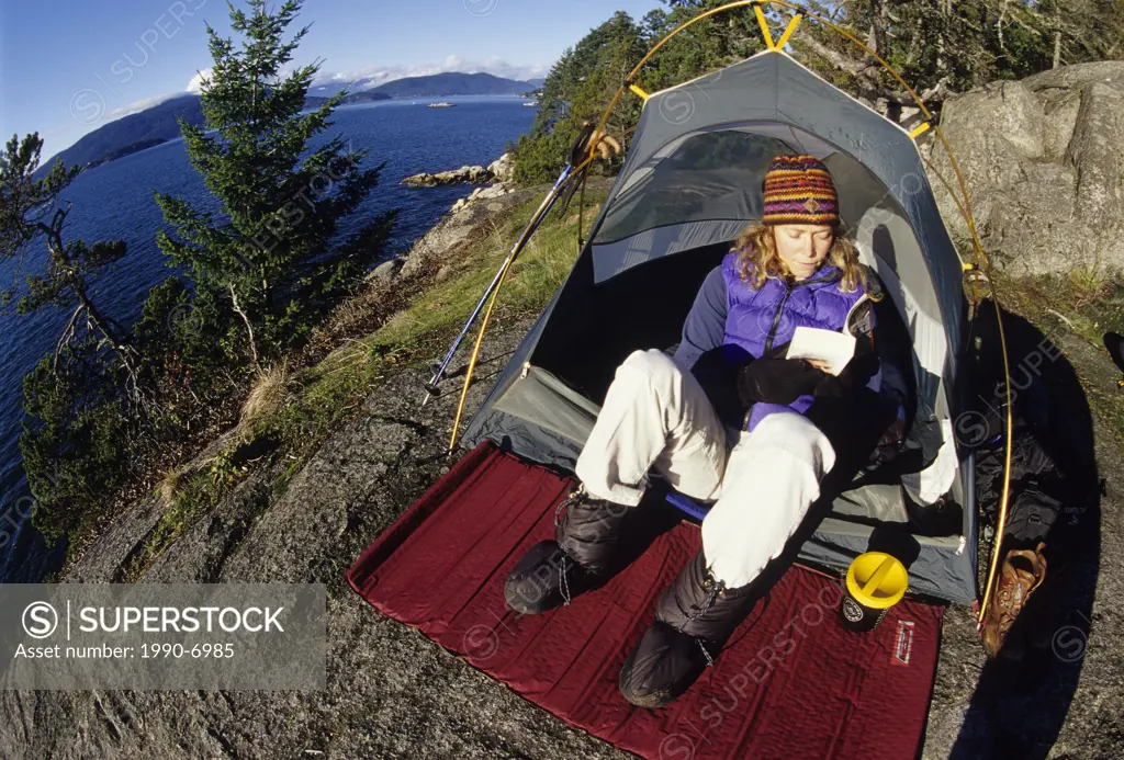 Woman reads a book in her tent, Lighthouse Park, West Vancouver, British Columbia, Canada.