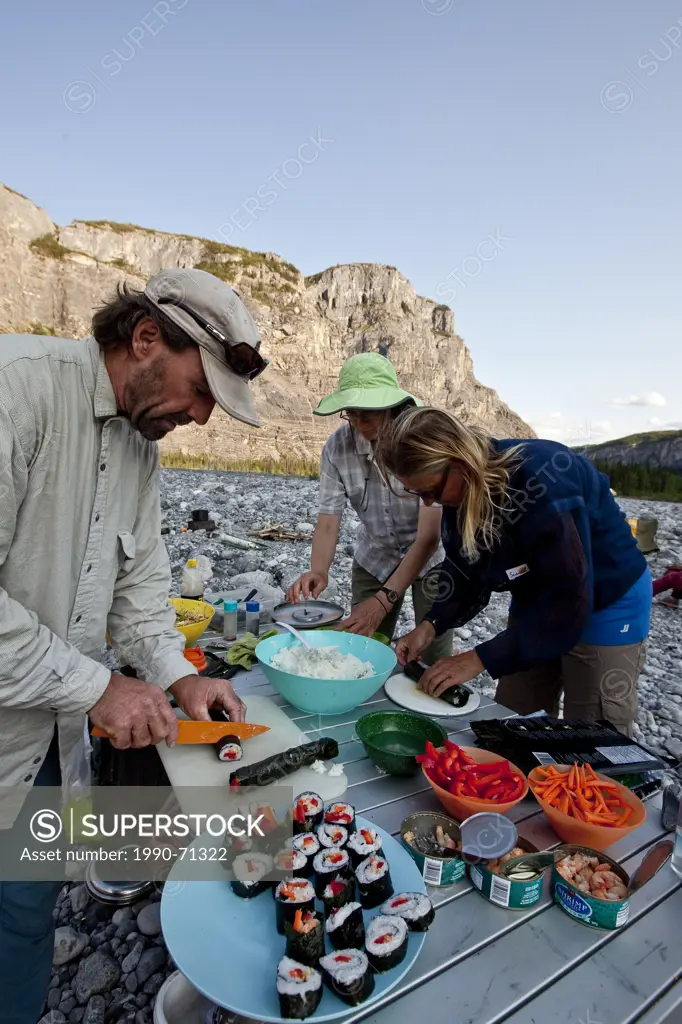 Three adults prepare sushi while camped on Nahanni River, Nahanni National Park Preserve, NWT, Canada.