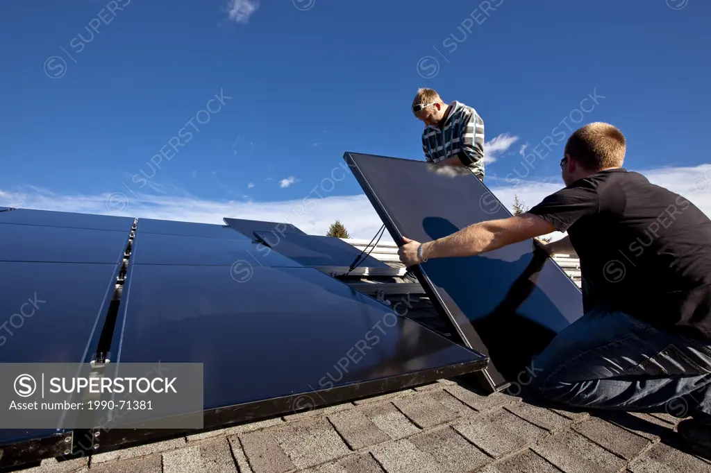 Two solar panel installers install solar panels on roof, Alberta foothills near Black Diamond, Alberta, Canada.