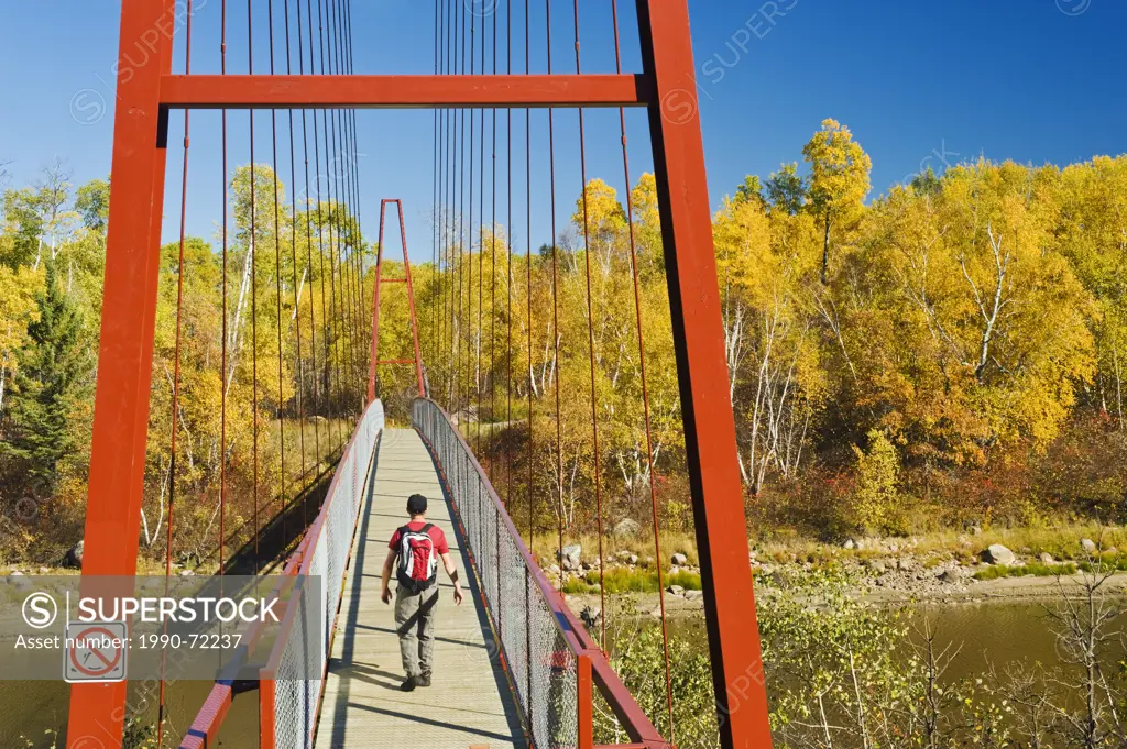 Hiker crosses a bridge over the Whiteshell River along the Trans Canada Trail, Whiteshell Provincial Park, Manitoba, Canada