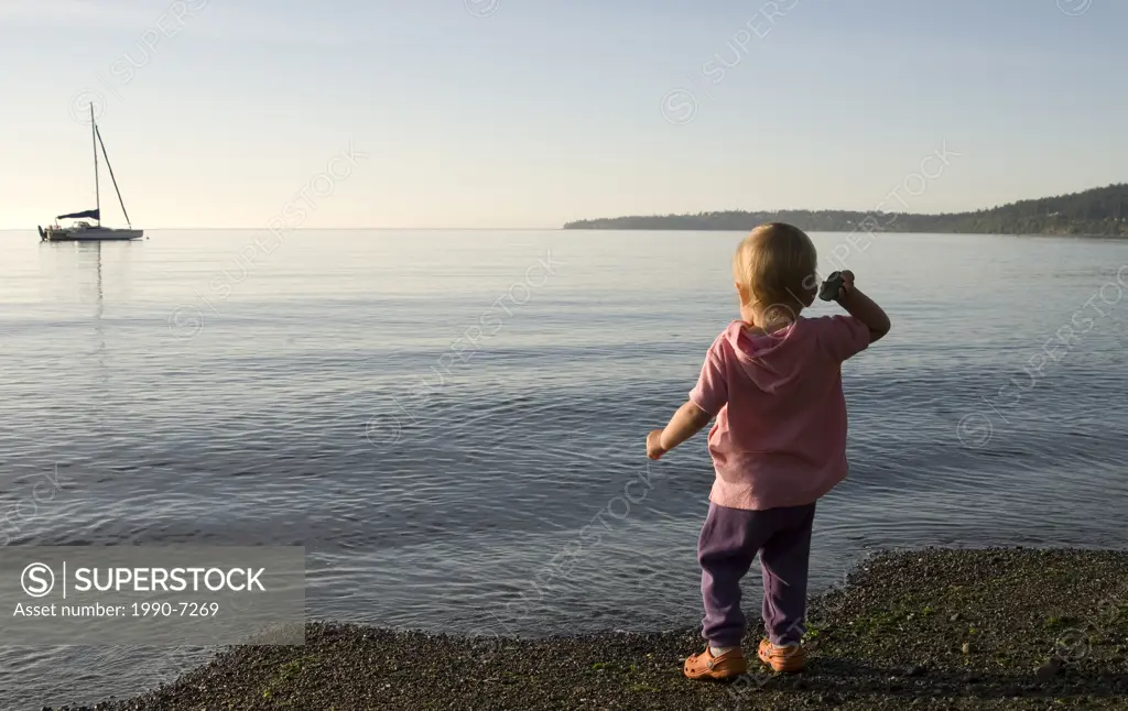 Young girl throws stones on beach near Cordova Bay, Victoria, Vancover Island, British Columbia, Canada