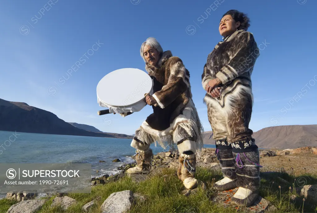 Inuit couple in traditional caribou skins drum dancing and singing, Devon Island, Nunavut, Canada