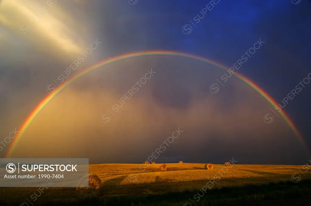 Rainbow and bales after prairie storm at sunset near Cypress River, Manitoba, Canada