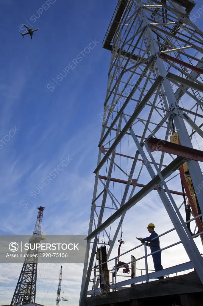 Oil drilling rig worker with airplane flying overhead, Alberta, Canada