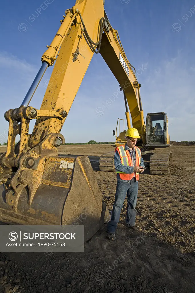 Middle age male grader operator texting on cell phone, Alberta, Canada