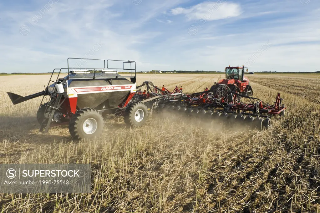 moving tractor and and air till seeder planting winter wheat in a zero till canola stubble field, Lorette, Manitoba, Canada