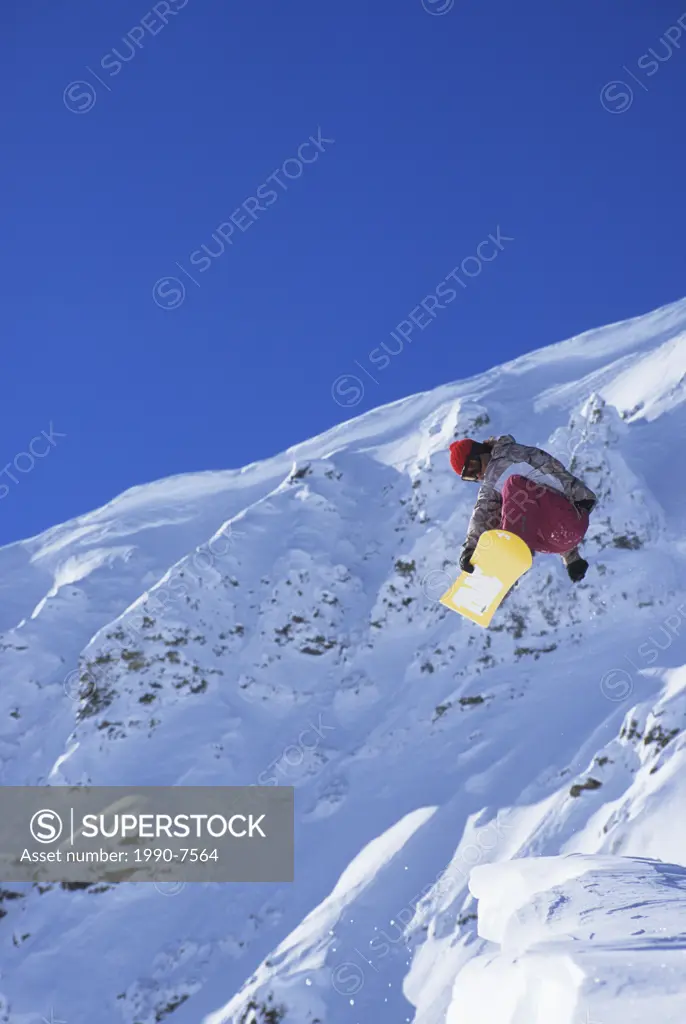 Young female snowboarder jumping off a cornice in the backcountry  Golden, British Columbia, Canada