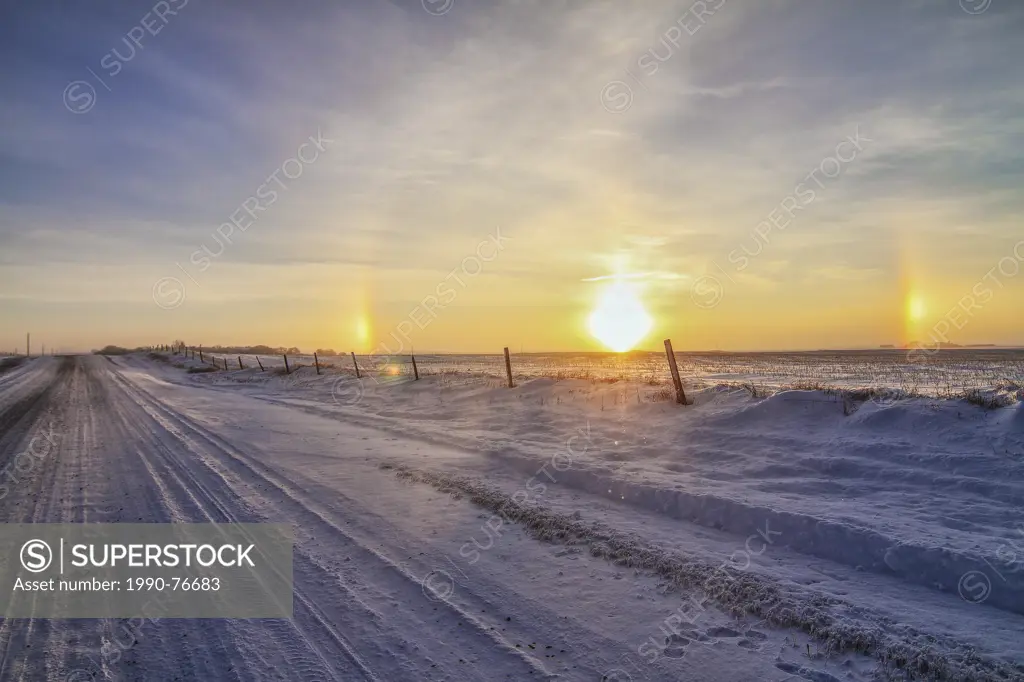 Rural road and fence line, in winter, with sun and dual rainbows to the side. Strathmore, Alberta, Canada