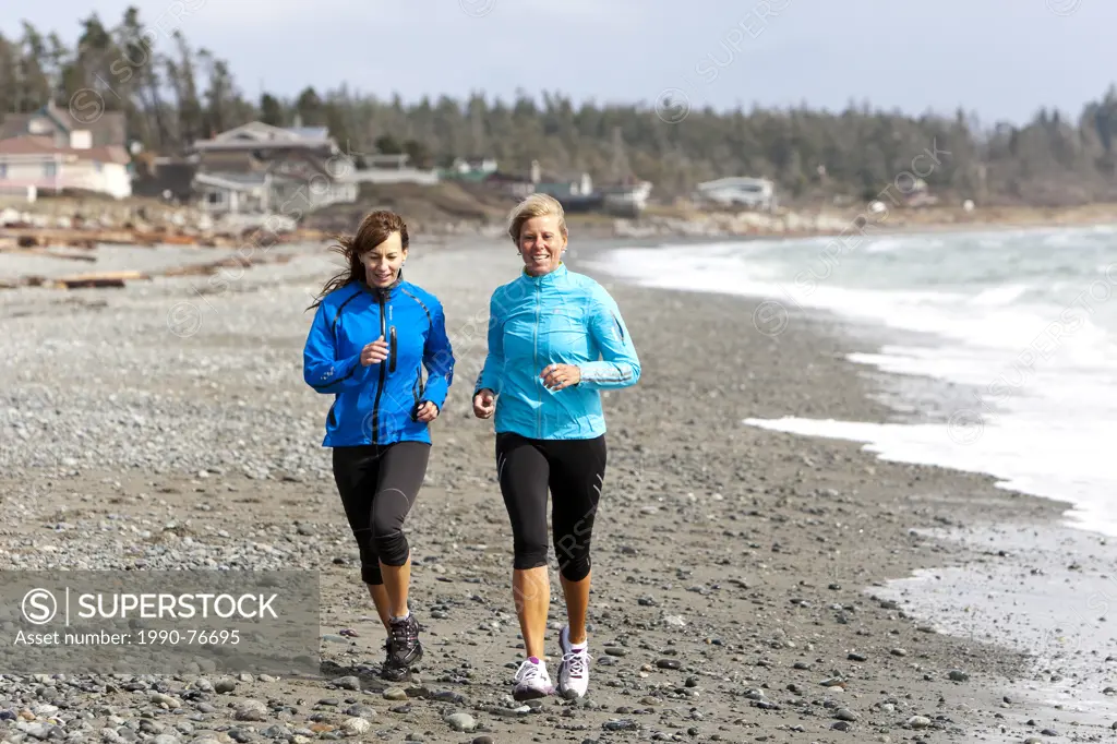 Two friends run along the beach at Cape Lazo near Comox in the Comox Valley. Comox, The Comox Valley, Vancouver Island, British Columbia, Canada.