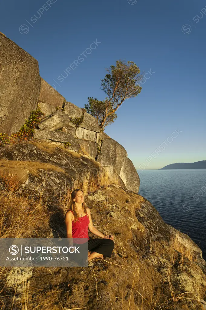 A young woman meditates along the bluffs of Stillwater, near Powell River. Stillwater Bluffs, The Sunshine Coast, ,British Columbia, Canada.