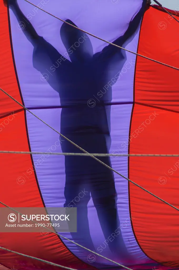 A parasailing crew member is silhouetted holding a parachute preparing to lift a client skyward off the Vietnamese coast of Nha Trang, Socialist Repub...