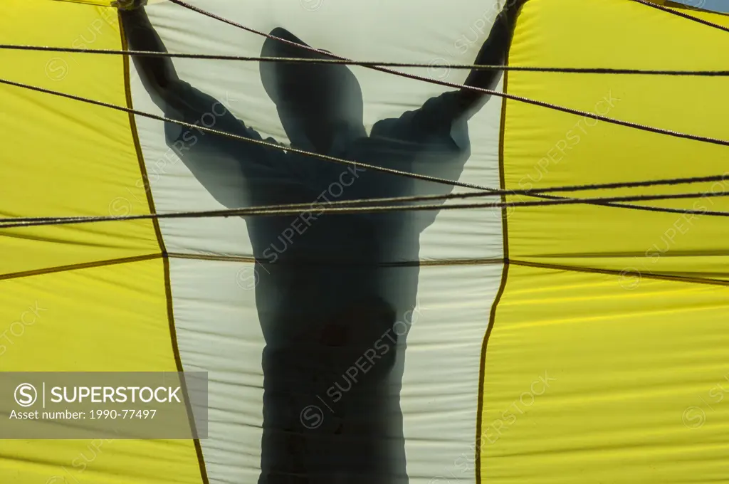 A parasailing crew member is silhouetted holding a parachute preparing to lift a client skyward off the Vietnamese coast of Nha Trang, Socialist Repub...