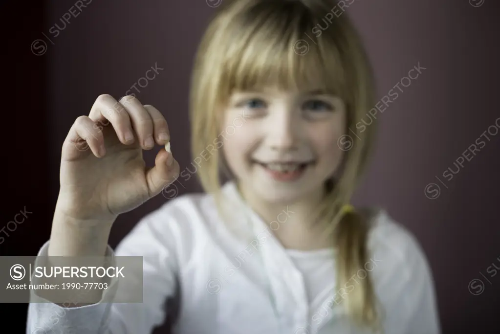 Smiling little girl showing her first loose tooth with focus on the tooth