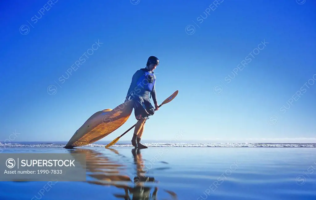 Man pulling kayak on to beach, Tofino, Vancouver Island, British Columbia, Canada