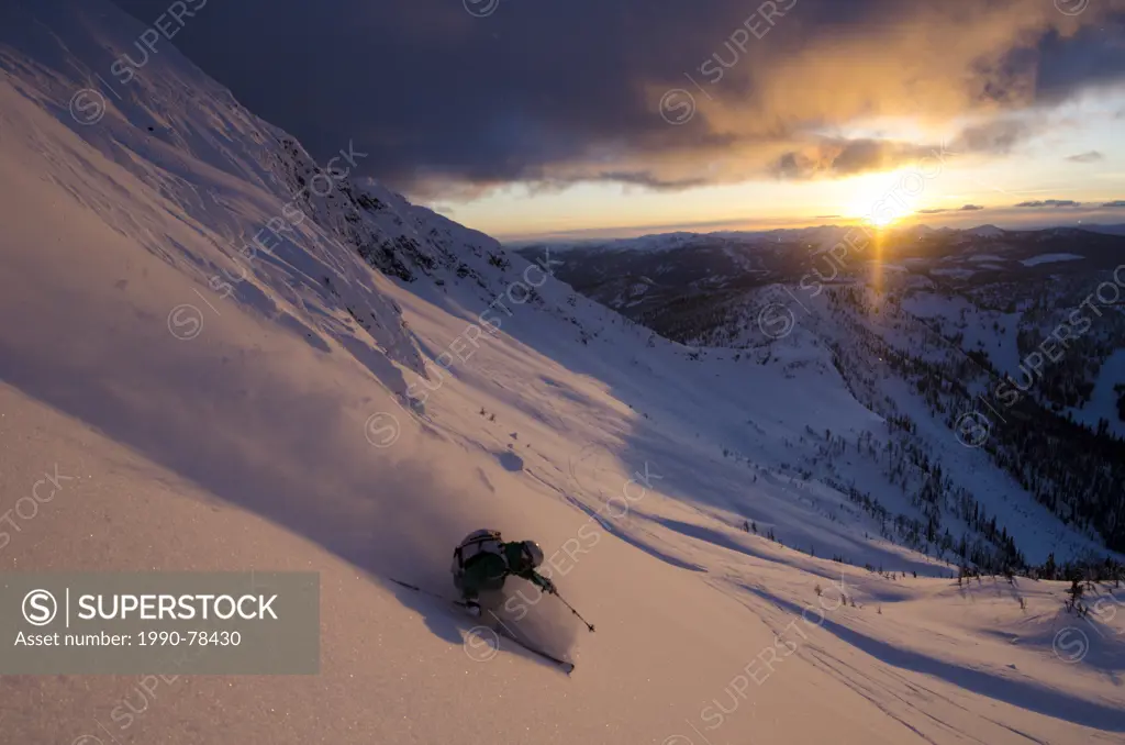A female skier turning in the alpenglow below Ymir Peak in the Whitewater backcountry near Nelson, British Columbia