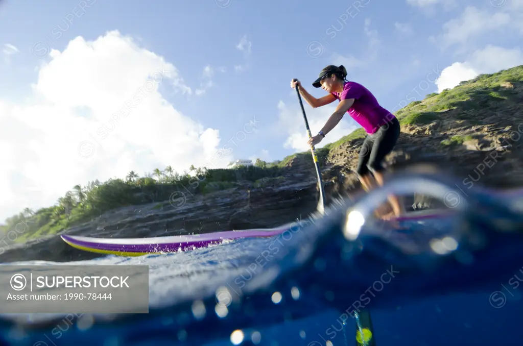 A woman paddles on her stand-up paddleboard off the cliffs of Honolulu, Oahu, Hawaii