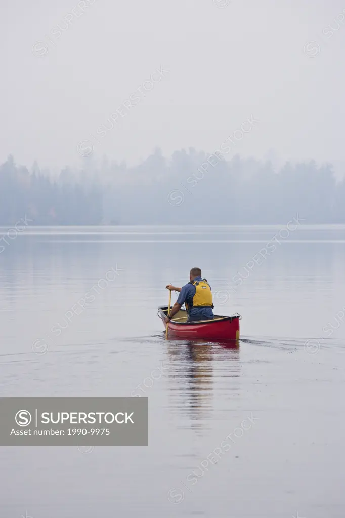 Young/middle_aged man canoes out on Source Lake with fishing rod, Algonquin Provincial Park, Ontario, Canada.