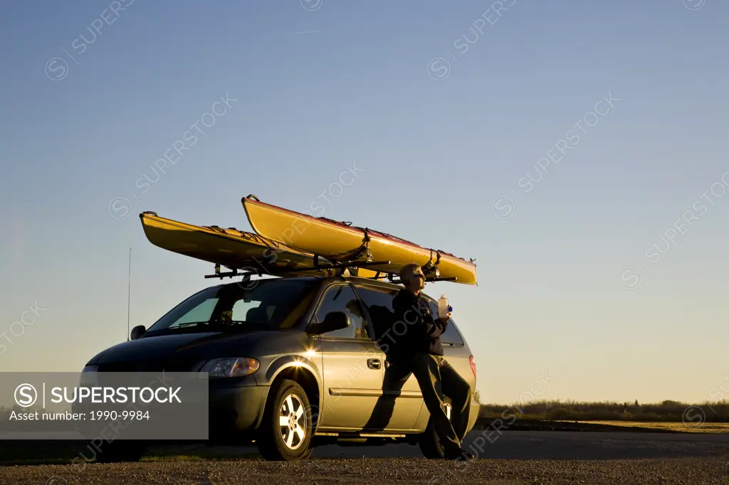 Man relaxes by van with sea kayaks near Lake Superior, Ontario, Canada.