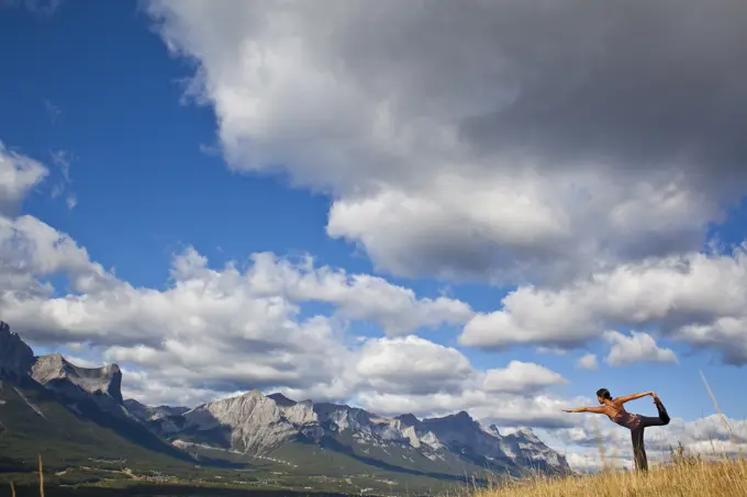 A young woman practicing yoga on a hill above the town of Canmore, AB