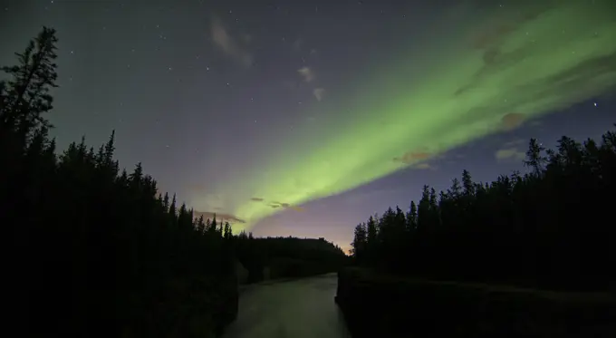 The aurora borealis or northern lights light up the night sky over top of the Yukon River as it flows through Miles Canyon, Whitehorse, Yukon.