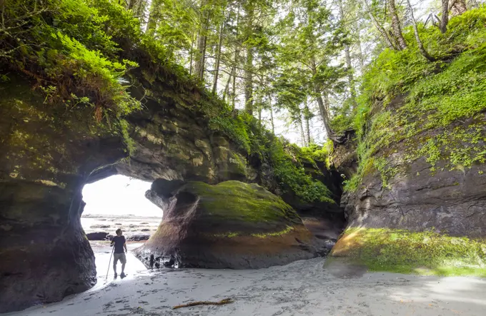 A hiker stands in the opening of a sea cave at Owen Point along the West Coast Trail. Pacific Rim National Park Reserve, Vancouver Island, BC, Canada.