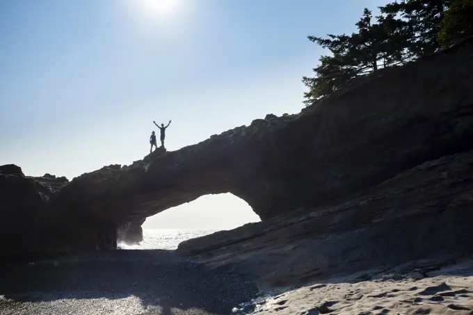 Two hikers stand on top of the sea arch at Tsusiat Point known as the 'Hole in the Wall'. West Coast Trail, Pacific Rim National Park Reserve, Vancouv...