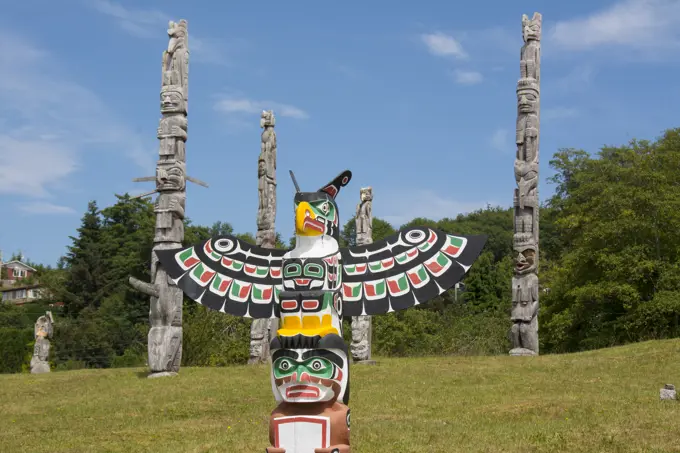 Thunderbird and Man holding copper by Bruce Alfred, older poles behind, at Namgis Burial grounds, Alert Bay, Cormorant Island, Vancouver Island, Briti...