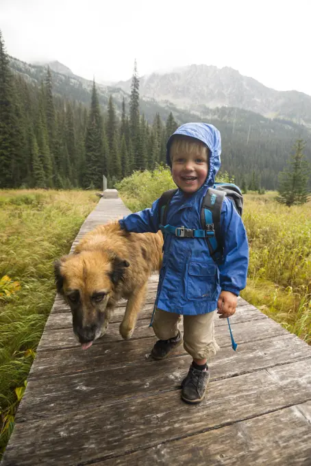 A happy toddler (boy) and his dog hikes on a boardwalk around Gibson Lake in Kokanee Glacier Provincial Park, British Columbia