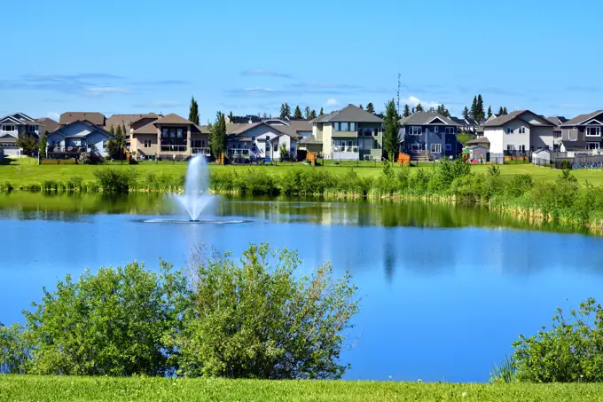 An urban landscape with a green space ,pond, houses and blue sky in Morinville Alberta Canada.