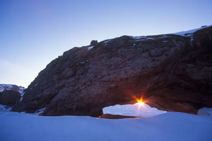 The sun sets under an arch at the geological formation known as The Arches Provincial Park, Great Northern Peninsula . Newfoundland and Labrador, Canada.